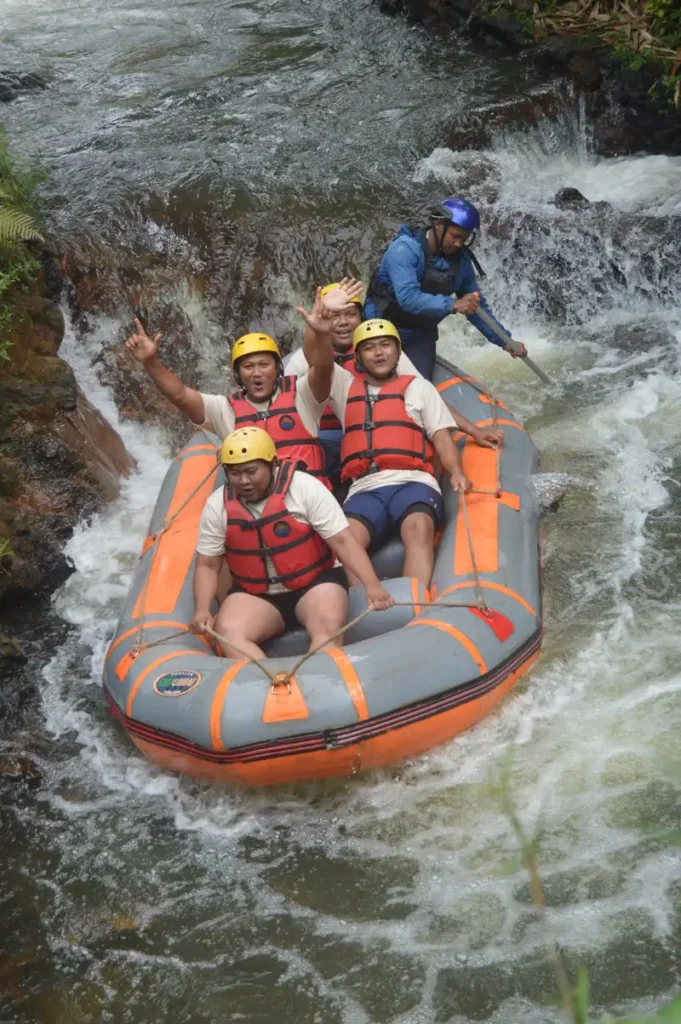Rombongan Bank Jakarta memasuki salah satu jeram Sungai Palayangan; guide FAST Rafting berdiri mengendalikan perahu dari belakang sementara peserta berseragam putih duduk bersorak menyambut jeram.